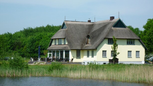 Una casa grande con techo de paja, un porche y vistas a un lago.