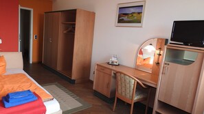 A hotel room with a bed, a wardrobe, a desk with a chair, a television, and a framed picture on the wall. - Double room Cat. I - Double Room Golf-Centrum Schloss Karnitz (Garz/Rügen)
