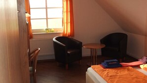 Una habitación pequeña y acogedora con una cama, dos sillas, una mesita y una ventana con cortinas.