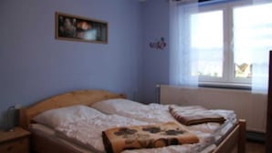 A bedroom with a double bed, a nightstand, a window with curtains, and a radiator.