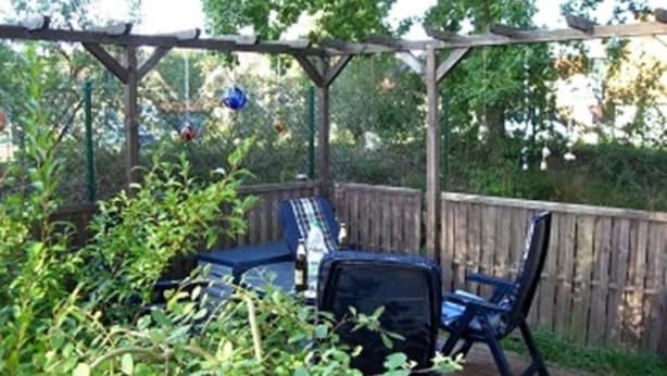 A covered patio with a wooden pergola, a table, and two chairs.