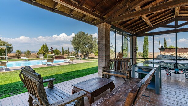 Eine überdachte Terrasse mit Holzmöbeln, einem Pool und Blick auf die Landschaft.