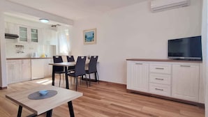 Una cocina compacta con comedor, muebles blancos, un televisor de pantalla plana y un cuadro en la pared.
