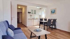Una sala de estar con sofá, una mesa de comedor con sillas y una cocina con armarios y fregadero.