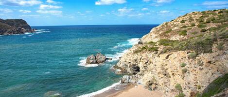 A coastal landscape with a beach, rocky cliffs, and the ocean.