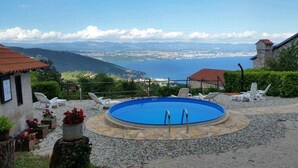 A pool area with a view of a coastal city, surrounded by greenery and stone pathways. - Holiday home with sea view and pool (Dobreć)