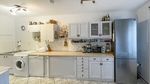 Una cocina compacta con armarios blancos, un refrigerador de acero inoxidable, una lavadora y un microondas.