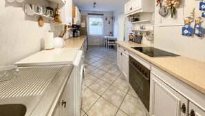 Cocina con armarios blancos, estufa y lavamanos. Se ve vegetación por la ventana.