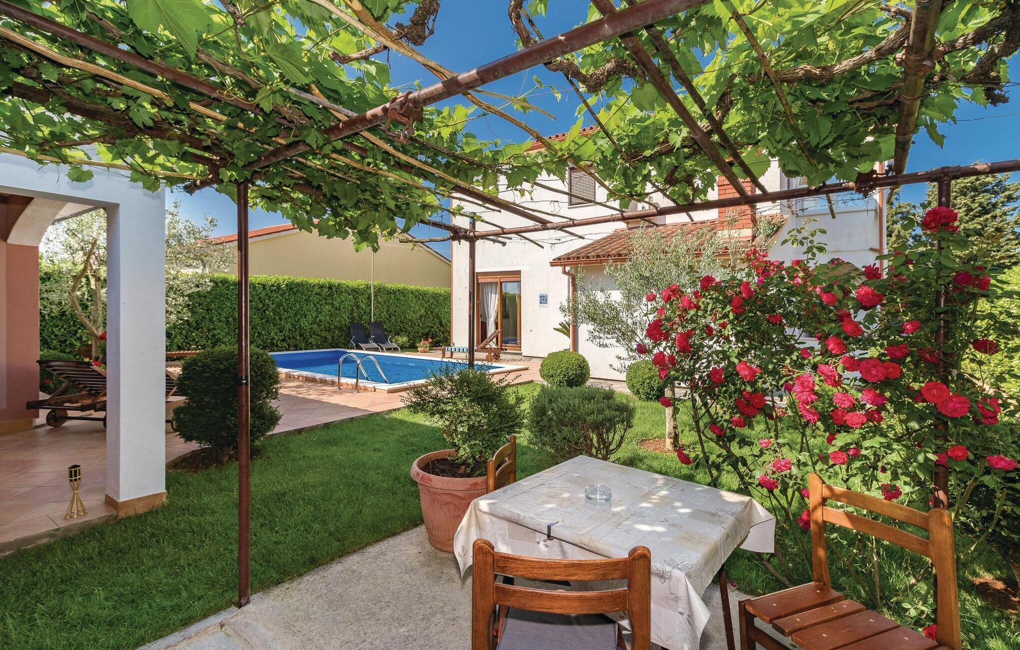 A private garden with a pool, a pergola with climbing plants, a table with chairs, and a rose bush.
