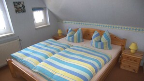 A double bed with striped bedding, two bedside tables with lamps, a window with a view, and a decorative wall piece. - Apartment 01 - Apartments Oechsner (Heringsdorf)