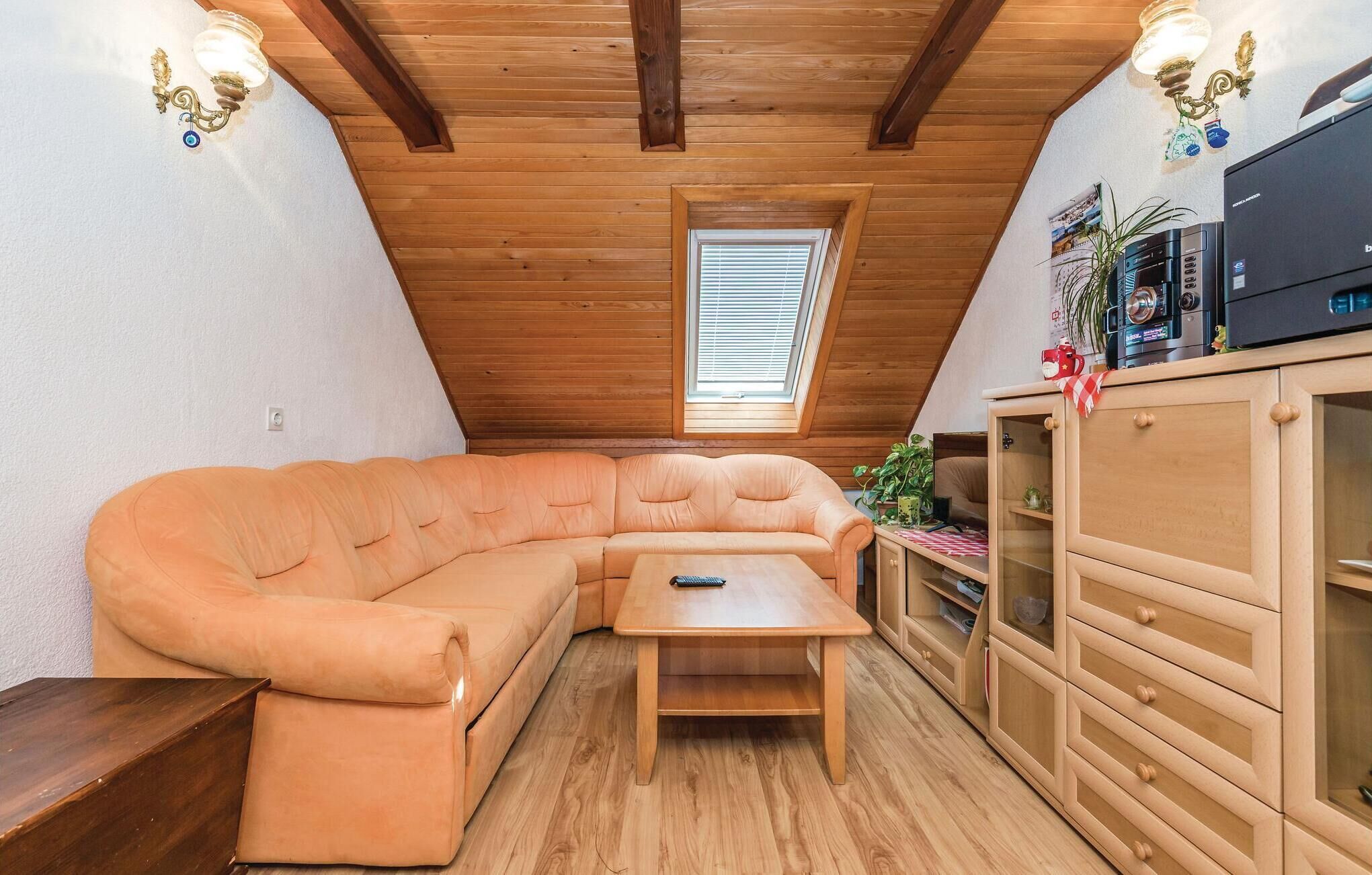 A cozy attic room with a wooden ceiling, a built-in sofa, a small table, and a cabinet with a TV.