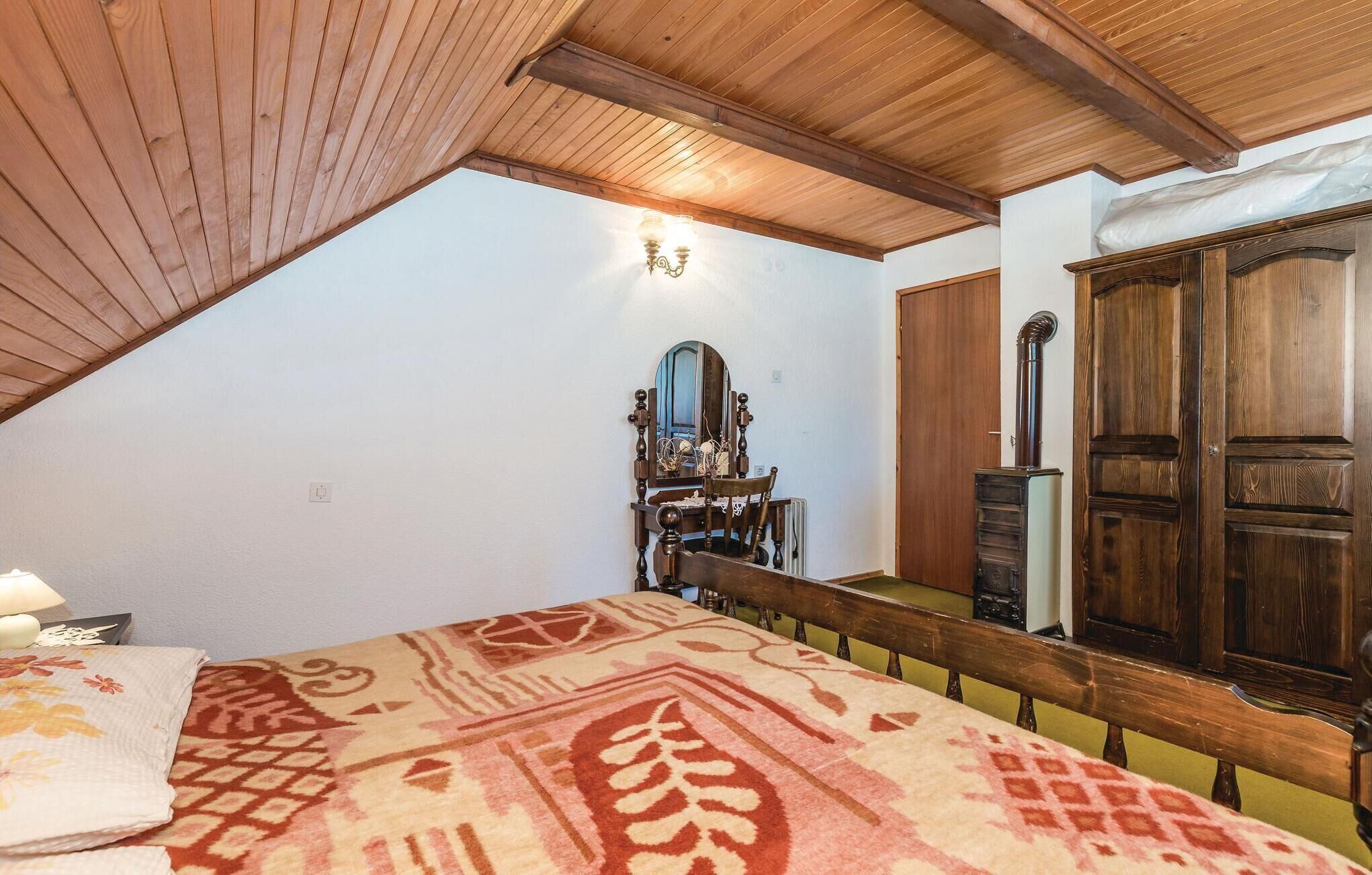 A bedroom with a sloped ceiling, a wooden bed, a dresser, a mirror, and a radiator.