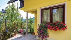 Un edificio amarillo con una ventana adornada con flores rojas y rosas, rodeado de follaje y plantas en macetas.