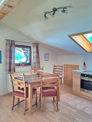 A dining area with a wooden table and chairs, a kitchen with a built-in oven, and a skylight.