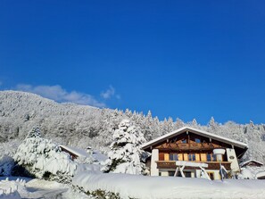 A snow-covered lodge with a wooden exterior, surrounded by snow-laden trees and a clear blue sky.