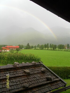A house with a red roof, a green field, and a mountain range in the background.