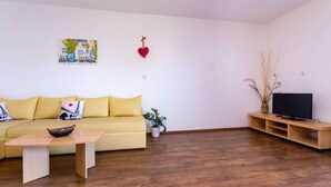 Una sala de estar con un sofá amarillo, una mesa de centro de madera, un televisor sobre un mueble de madera y un cuadro en la pared.