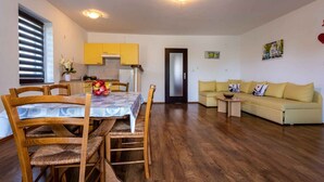 Una sala de estar moderna con un sofá y una mesa de comedor con sillas. Hay una zona de cocina con armarios amarillos y un refrigerador.