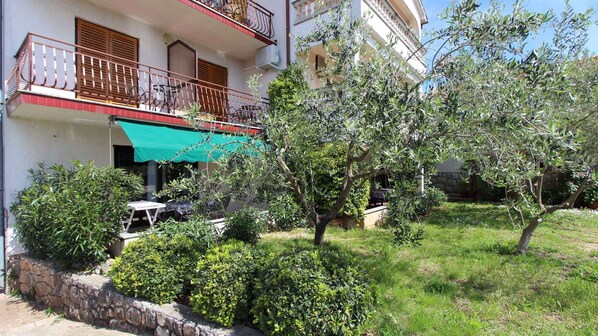 A building with a balcony, outdoor seating, and a garden with trees and shrubs.