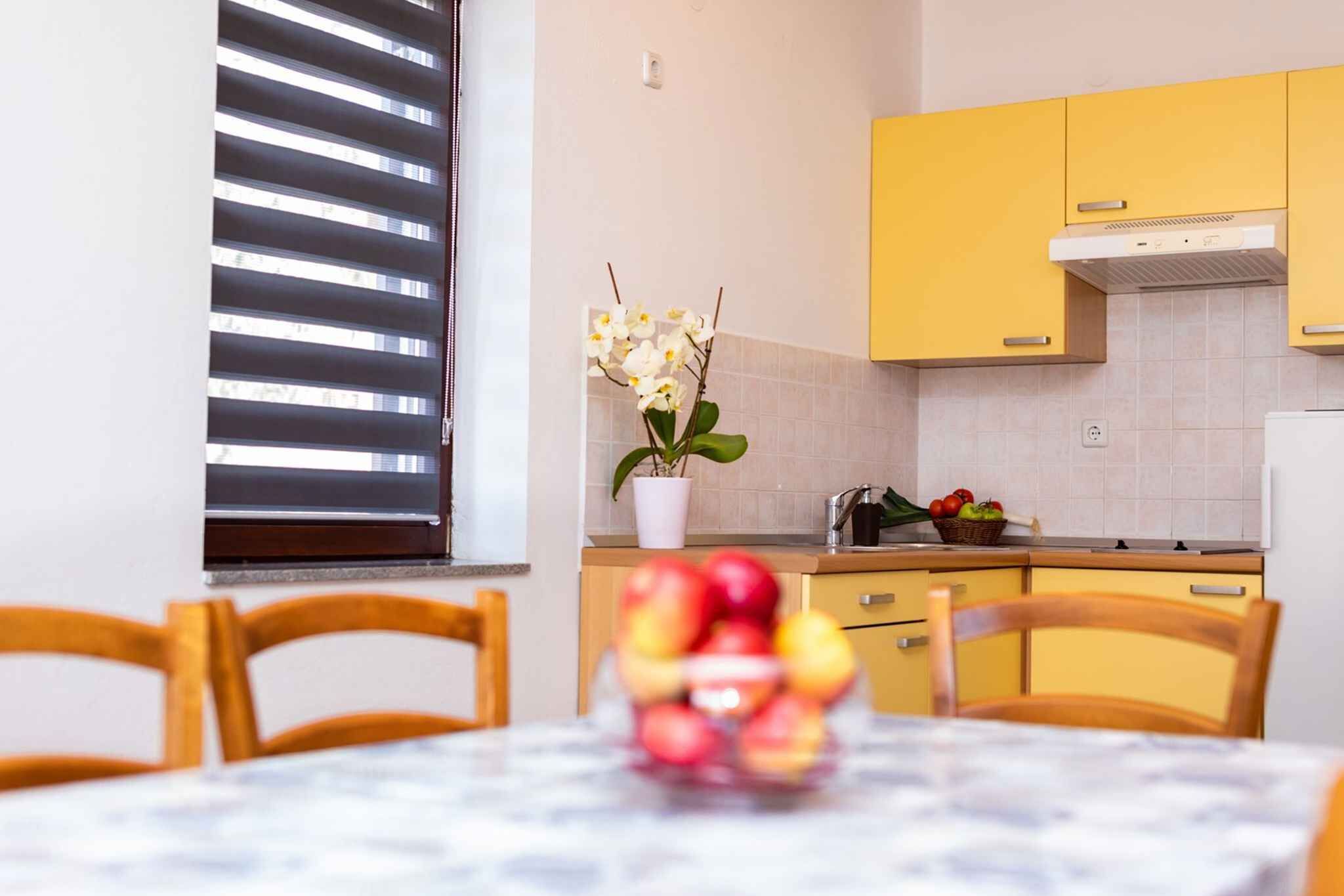 Una cocina con armarios amarillos, encimera blanca y una ventana con persianas.