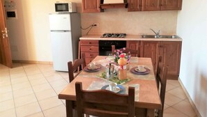 A kitchen with wooden cabinets, a white refrigerator, a stove, and a dining table set with plates, cups, and a bottle of juice. - Studio with air conditioning and pool (Ariano nel Polesine)