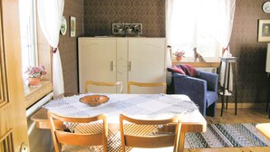 A dining area with a table set for four, wooden chairs, a cabinet with a clock, and a window with curtains.