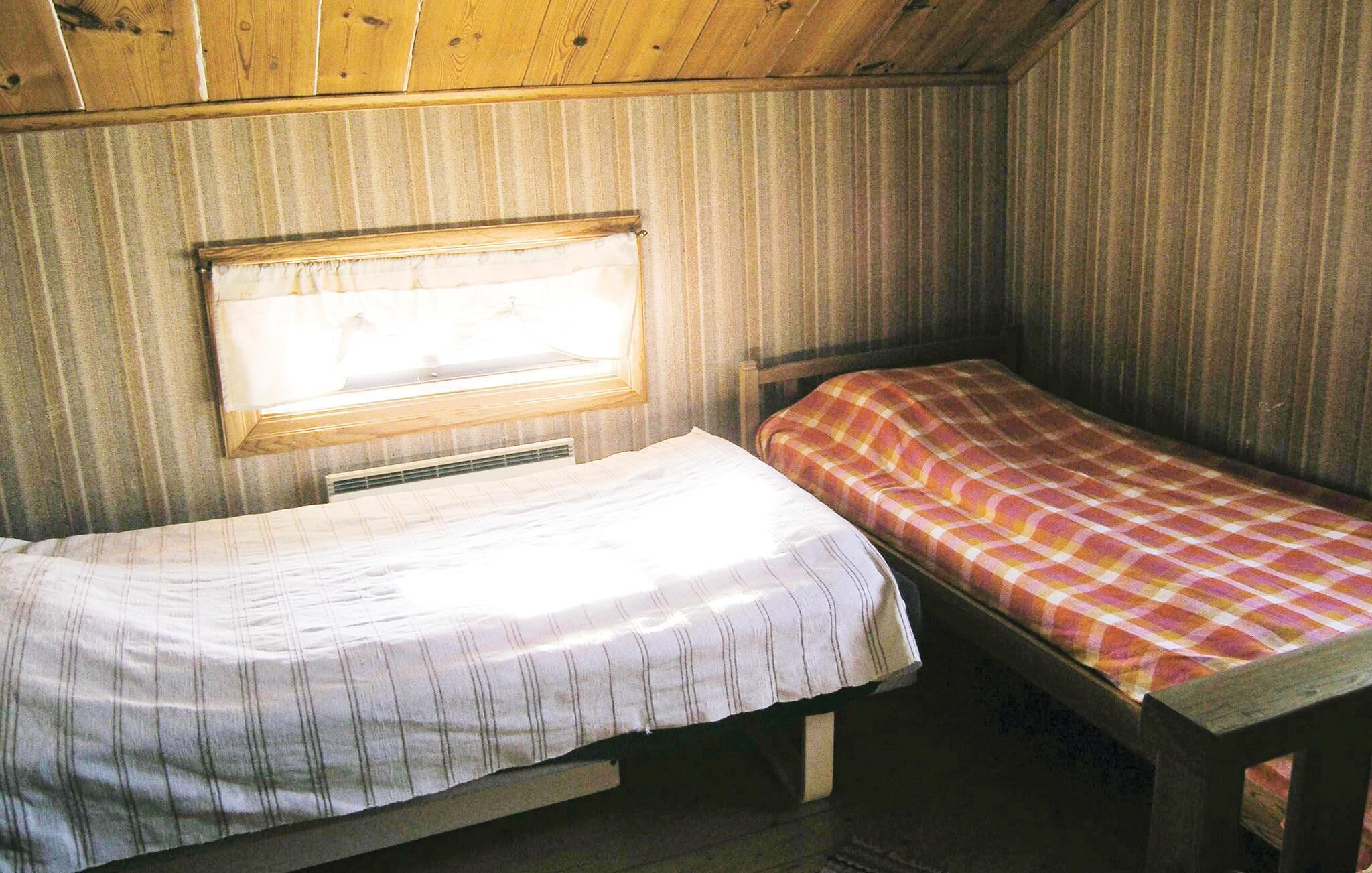 A small, cozy room with two single beds, a window, and wooden walls.