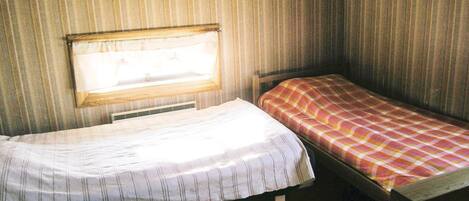 A small, cozy room with two single beds, a window, and wooden walls.