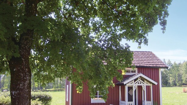 A red wooden building with a porch, a table, and two chairs.