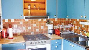 A compact kitchen with a gas stove, oven, and a coffee maker. There are cabinets with knobs, a sink, and a tiled backsplash.