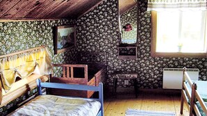 A rustic bedroom with a wooden bed, a small table, a chair, and a window with a view.
