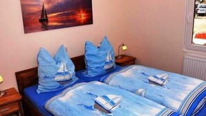 A bedroom with a bed covered in a blue and white striped blanket, a nightstand with a lamp, and a painting of a sailboat on the wall. - Tern (House 167) - FH 167 (Mönkebude)
