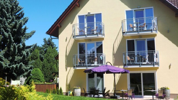 A two-story building with balconies, a patio area with outdoor furniture, and a well-maintained garden. - Double room 4 - PENSION Delia Will in Ahlbeck (Heringsdorf)