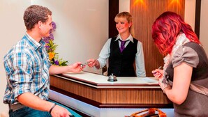 A reception desk with a bell, a man handing over a key, and a woman receiving it. - Double room 4 - PENSION Delia Will in Ahlbeck (Heringsdorf)