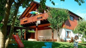 A house with a wooden balcony, a slide, and a child playing. - Apartment - Holiday apartments Haus Waldesruh (Edertal)