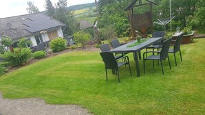 A patio with a table and chairs, surrounded by a well-maintained lawn and stone pathway. - Apartment - Holiday apartments Haus Waldesruh (Edertal)