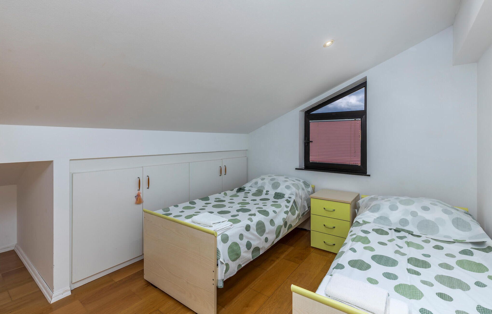 Una habitación pequeña y luminosa con dos camas individuales, una ventana con persianas y un armario.