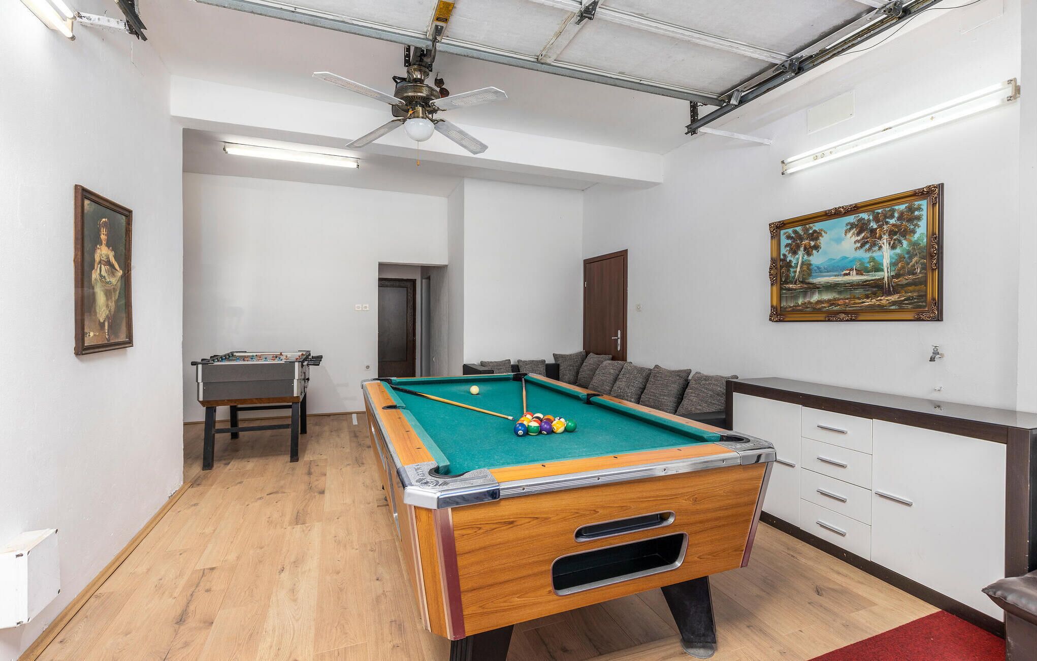 Une table de billard recouverte d’un drap vert, une table de baby-foot et un canapé avec des coussins.