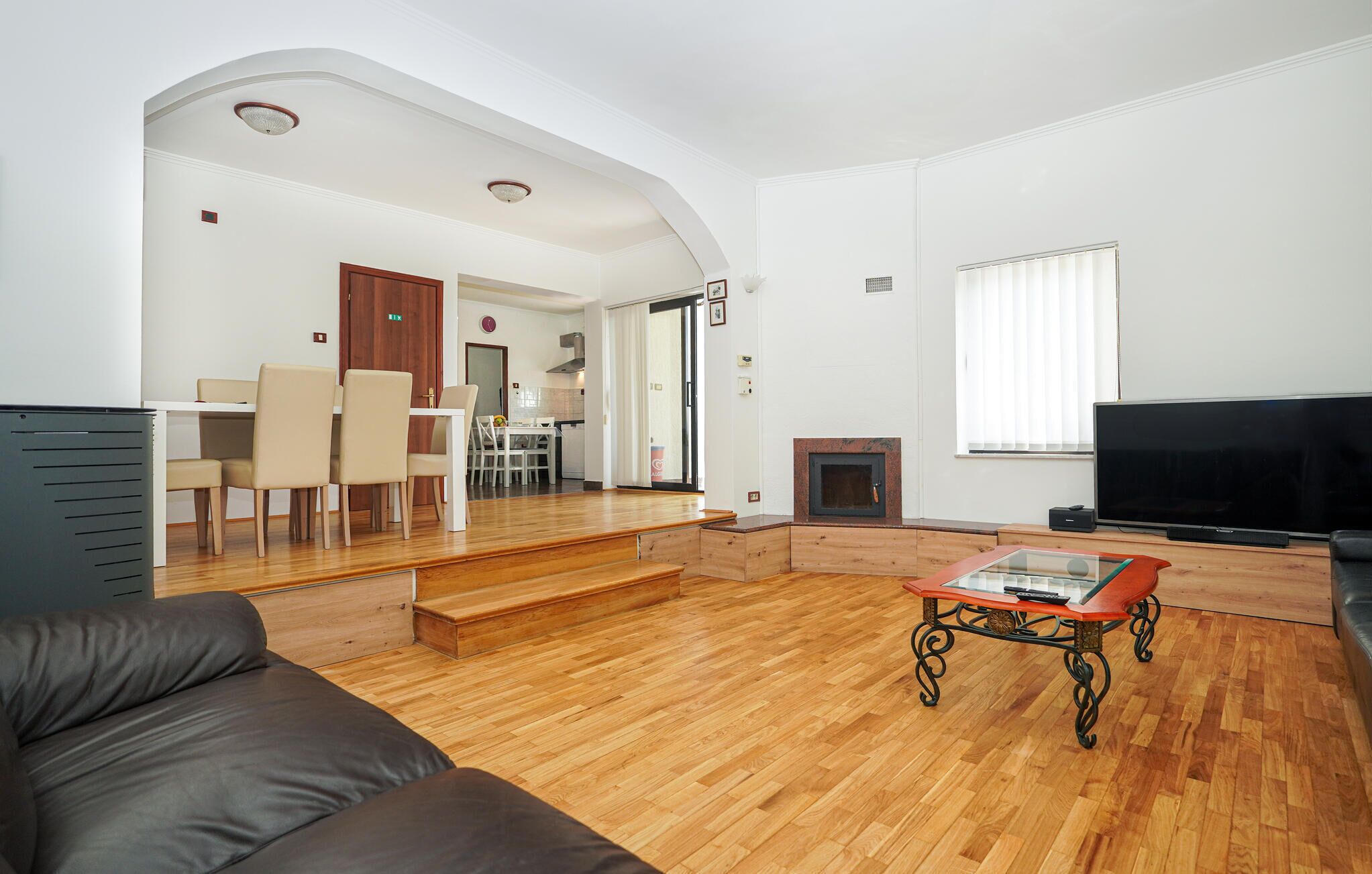 A living room with a wooden floor, a sofa, a glass-top coffee table, a fireplace, and a TV.