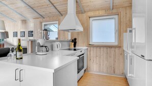 A modern kitchen with wooden paneling, white cabinetry, and a central island with a coffee maker and wine bottle. - Lovely home in Rømø with WiFi (Rømø)