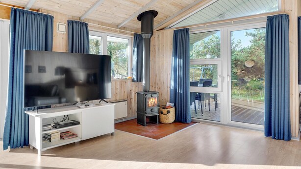 A modern living room with a large flat-screen TV, a wood-burning stove, and a glass door leading to an outdoor deck. - Lovely home in Rømø with WiFi (Rømø)