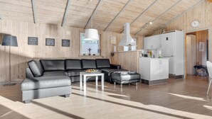 A modern living room with a black leather sofa, a white coffee table, and a kitchen area with a white refrigerator and cabinets. - Lovely home in Rømø with WiFi (Rømø)