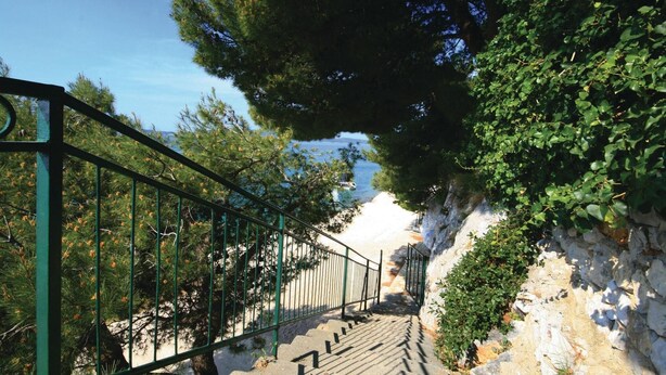 Un escalier menant à une plage, avec une rambarde d’un côté et un mur de pierre de l’autre.