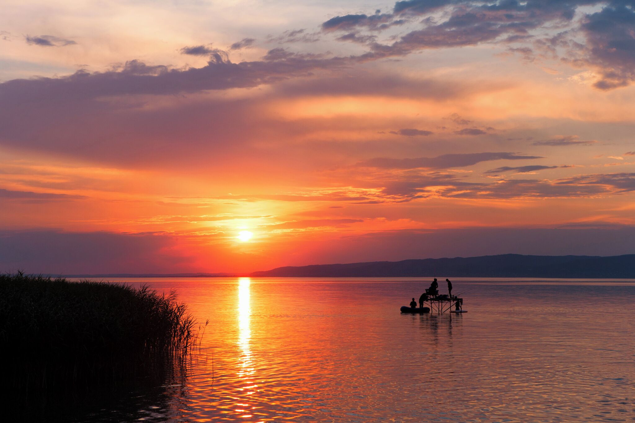 A sunset over a calm body of water with a dock and people on it.
