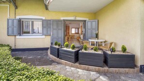 A courtyard with a dining area, built-in planters with small trees, and a covered entrance. - Studio 50 m from the shore of Lake Balaton, with pool (Balatonmáriafürdő)