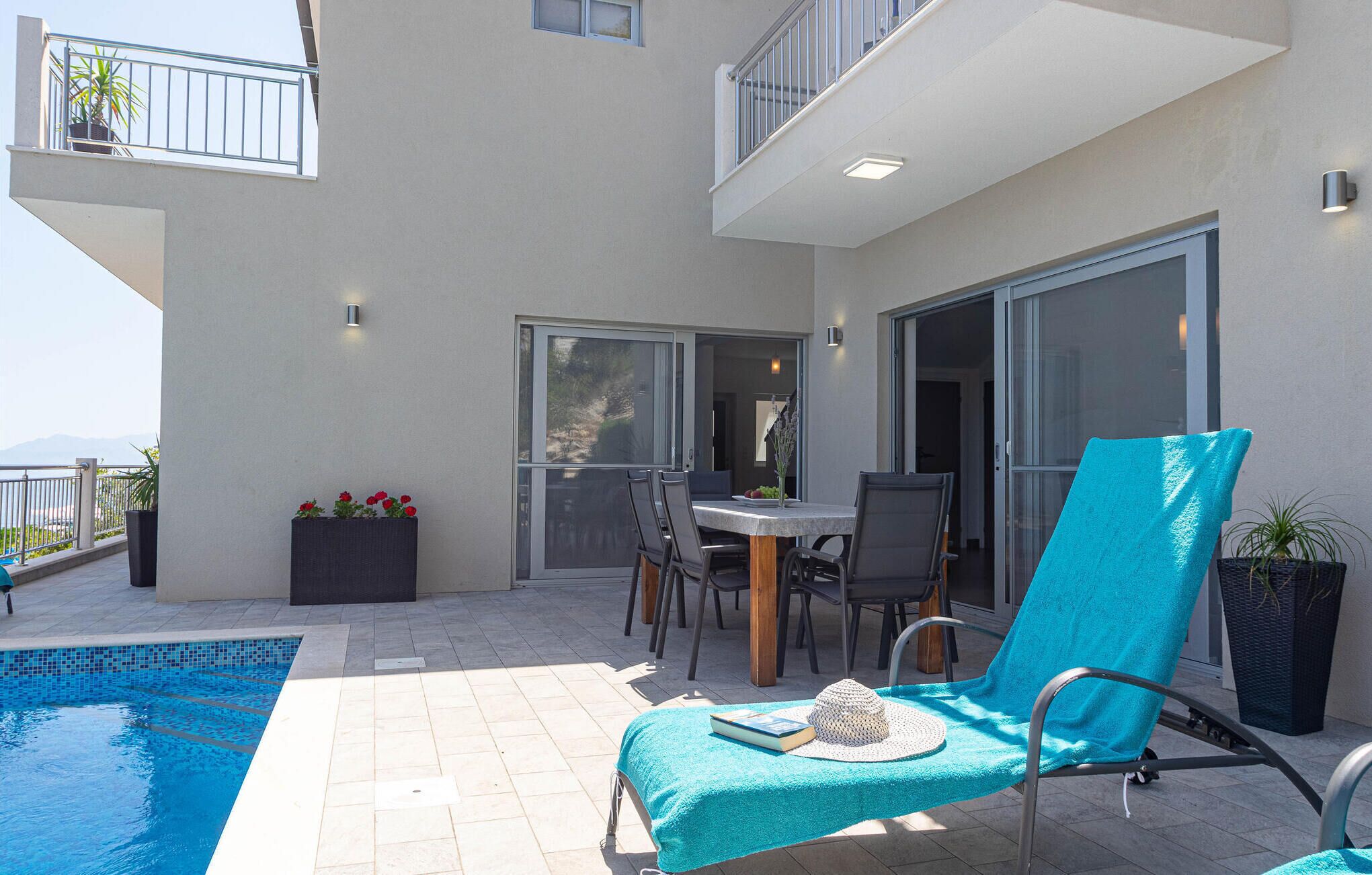 Un espacio exterior moderno con piscina, una mesa de comedor con sillas y una tumbona con toalla.