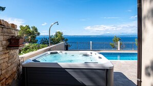 Ein Whirlpool mit Blick auf das Meer, eine Steinsäule und ein Metallgeländer.