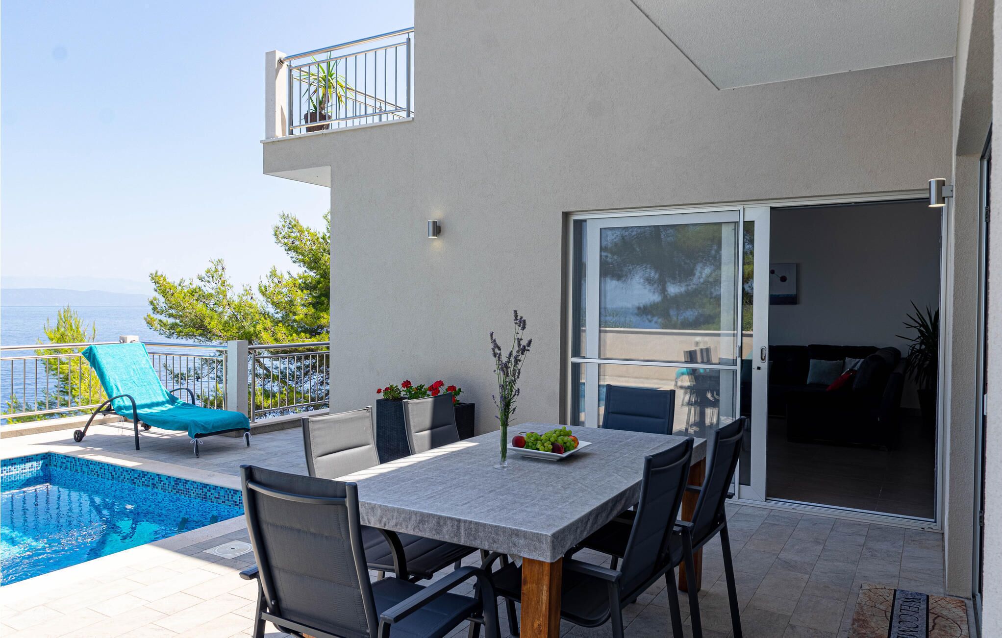 A balcony with a pool, outdoor seating, and a view of the sea.