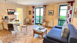 Una sala de estar con un sofá, una mesa de centro, una mesa de comedor con sillas, una zona de cocina y vistas a través de un ventanal grande.