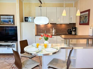 A modern kitchen with white cabinets, a wooden countertop, and a dining area with a round table set for two. - (210) 2-room apartment - apartment house Villa Laura (Kühlungsborn)
